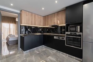 A modern kitchen with black and wooden cabinetry, a marble backsplash, and built-in appliances including a refrigerator, oven, and microwave.