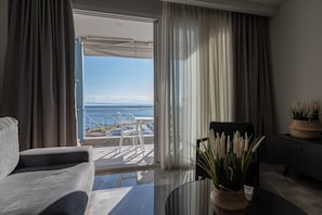A modern hotel room with a balcony, a sofa, a dining table, and a potted plant.