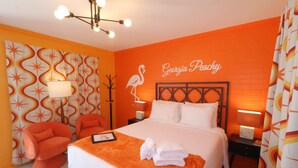 A hotel room with a bed, two nightstands, a lamp, a chair, and a wall with a flamingo design. - Georgia Peachy | Orange Boutique Retreat (Port Saint Joe)