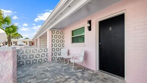 A pink building with a black door marked with the number 5, white chairs, and a patterned white fence. - Georgia Peachy | Orange Boutique Retreat (Port Saint Joe)