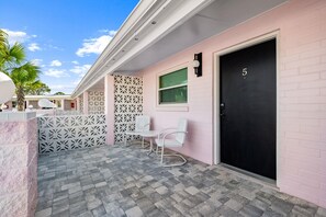 A pink building with a black door marked with the number 5, white chairs, and a patterned white fence. - Georgia Peachy | Orange Boutique Retreat (Port Saint Joe)