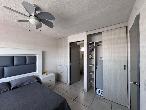Ein Schlafzimmer mit Bett, Nachttisch, Kleiderschrank und einem sichtbaren Badezimmer durch eine geöffnete Tür.