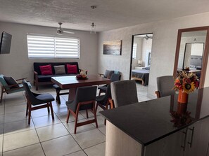 Ein modernes Wohnzimmer mit Essbereich, einer Couch mit Kissen, einem Fernseher und einem Deckenventilator.