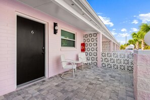 Een roze gebouw met een zwarte deur waarop het cijfer 6 staat, witte stoelen en een hekwerk met een patroon.