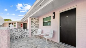 A building with a pink exterior, a black door marked with the number 7, and two white chairs outside. - Violet Valentino | Purple Boutique Retreat (Port Saint Joe)