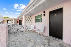 A building with a pink exterior, a black door marked with the number 7, and two white chairs outside. - Violet Valentino | Purple Boutique Retreat (Port Saint Joe)