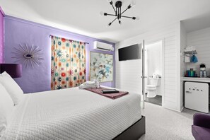 Un dormitorio con cama, televisor, aire acondicionado y baño visible a través de una puerta abierta.
