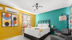 Ein Schlafzimmer mit einem Bett, einem Sessel, einem Nachttisch, einer Lampe und einer Wand mit geometrischem Muster.