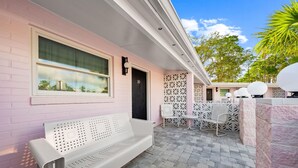 A pink building with a white bench, a door marked '10', and a white outdoor seating area with patterned walls. - Miss Pinky La Rue | Signature Pink Studio (Port Saint Joe)