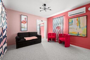 Une pièce avec un canapé noir, des fauteuils rouges, des murs roses, un luminaire au plafond et un grand tableau abstrait.