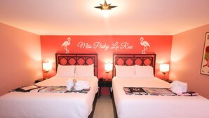 A hotel room with two beds, each with a nightstand, a lamp, and a framed picture. The room has a red accent wall with a sign above the beds. - Miss Pinky La Rue | Signature Pink Studio (Port Saint Joe)