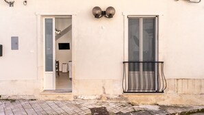 A building with two doors, a small balcony with a metal railing, and a tiled pavement. - La Capinera by Wonderful Italy (Noto)