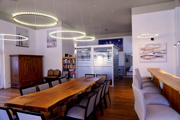 A dining area with a wooden table and chairs, pendant lights, a bookshelf, and a cabinet.