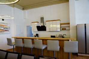 A modern kitchen with a bar area, white cabinetry, and a stainless steel refrigerator.