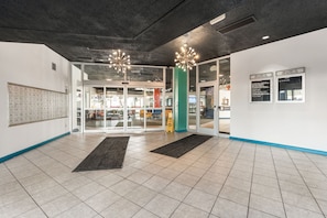 Un hall d’entrée moderne avec un sol carrelé, des portes en verre et un panneau d’affichage fixé au mur.