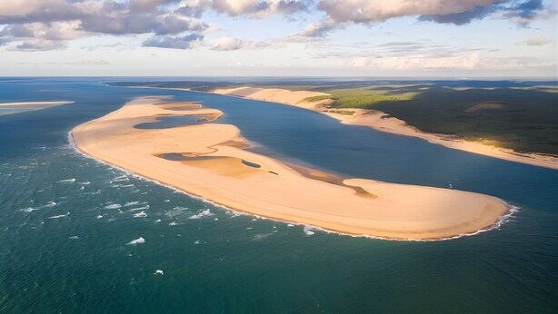 Vue aérienne d’un paysage côtier avec une plage de sable, des eaux bleues et limpides et une végétation verdoyante.