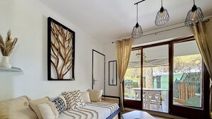 A modern living room with a sofa, a dining table, and a large window with a view of the outdoors. - LA PINEDA 200m from the naturist village with parking space and swimming pool (Occitanie)