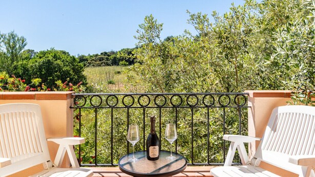 Een balkon met een tafel, twee stoelen en een fles wijn.