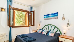 Een slaapkamer met een bed, een raam met gordijnen, een schilderij en een nachtkastje.
