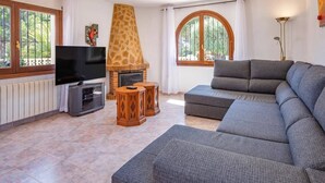 A living room with a television, sofa, fireplace, and large windows. - Villa Papillon by Villa Plus (Calp)