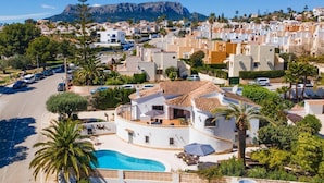 A residential area with a pool, white buildings, and a mountain in the background. - Villa Papillon by Villa Plus (Calp)