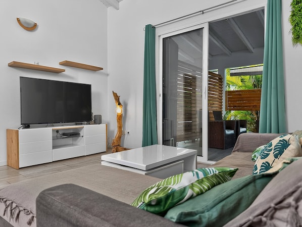 Una sala de estar moderna con una televisión de pantalla plana, muebles blancos y una mesa de centro de vidrio.