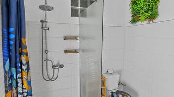 Ein Badezimmer mit einer Duschkabine, einer Toilette mit dekorativem Sitz und einer an der Wand befestigten Pflanze.