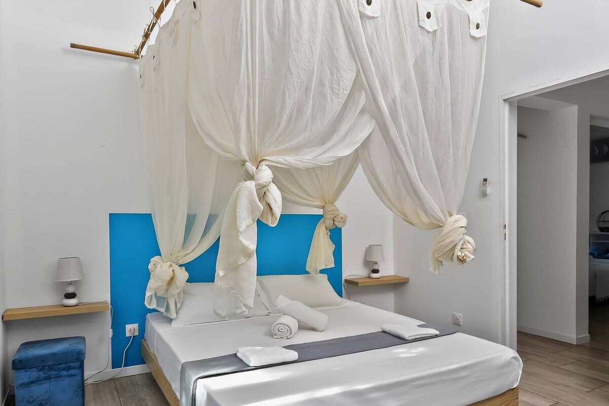 Un dormitorio con cama, mesitas de noche, lámparas de noche, una pared de acento azul y dosel sobre la cama.