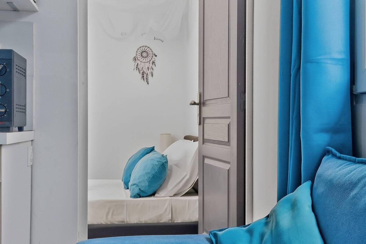 Una habitación con una cama, un sofá azul, una puerta blanca y una pared con un atrapasueños.