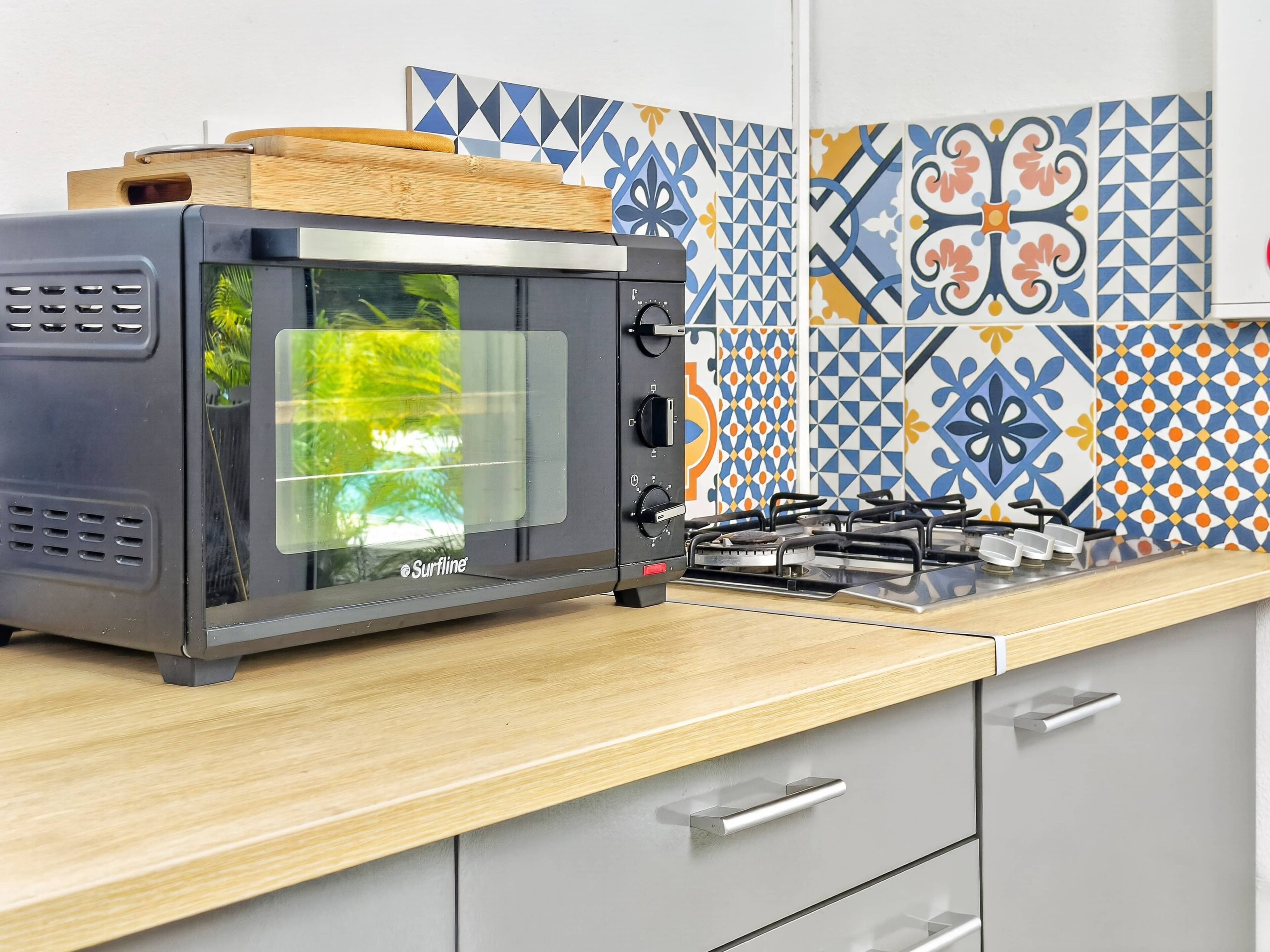 Een keuken met een Surfline magnetron, een gasfornuis en een houten snijplank.