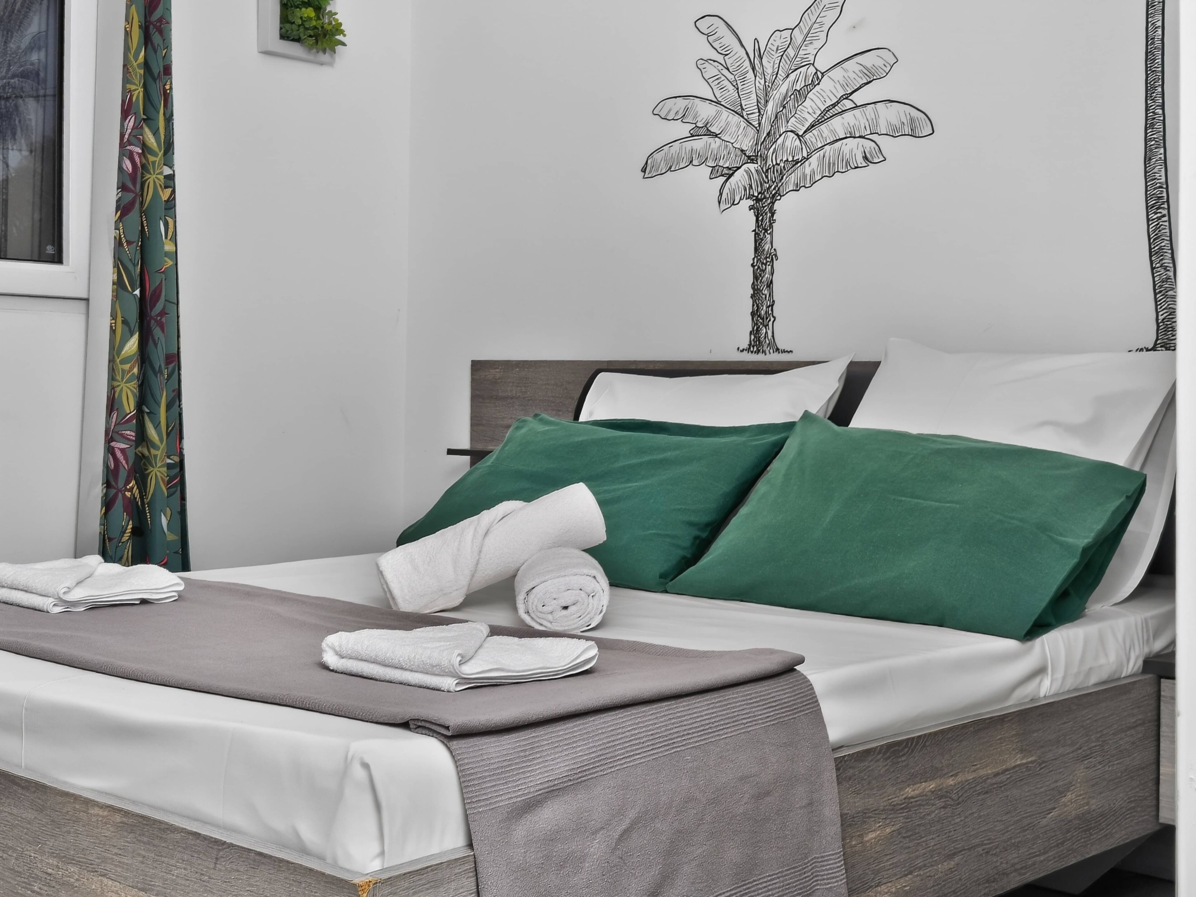 Un letto rifatto con cuscini verdi e bianchi, una coperta grigia e asciugamani arrotolati bianchi.