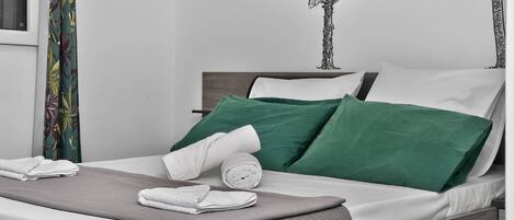 Un letto rifatto con cuscini verdi e bianchi, una coperta grigia e asciugamani arrotolati bianchi.