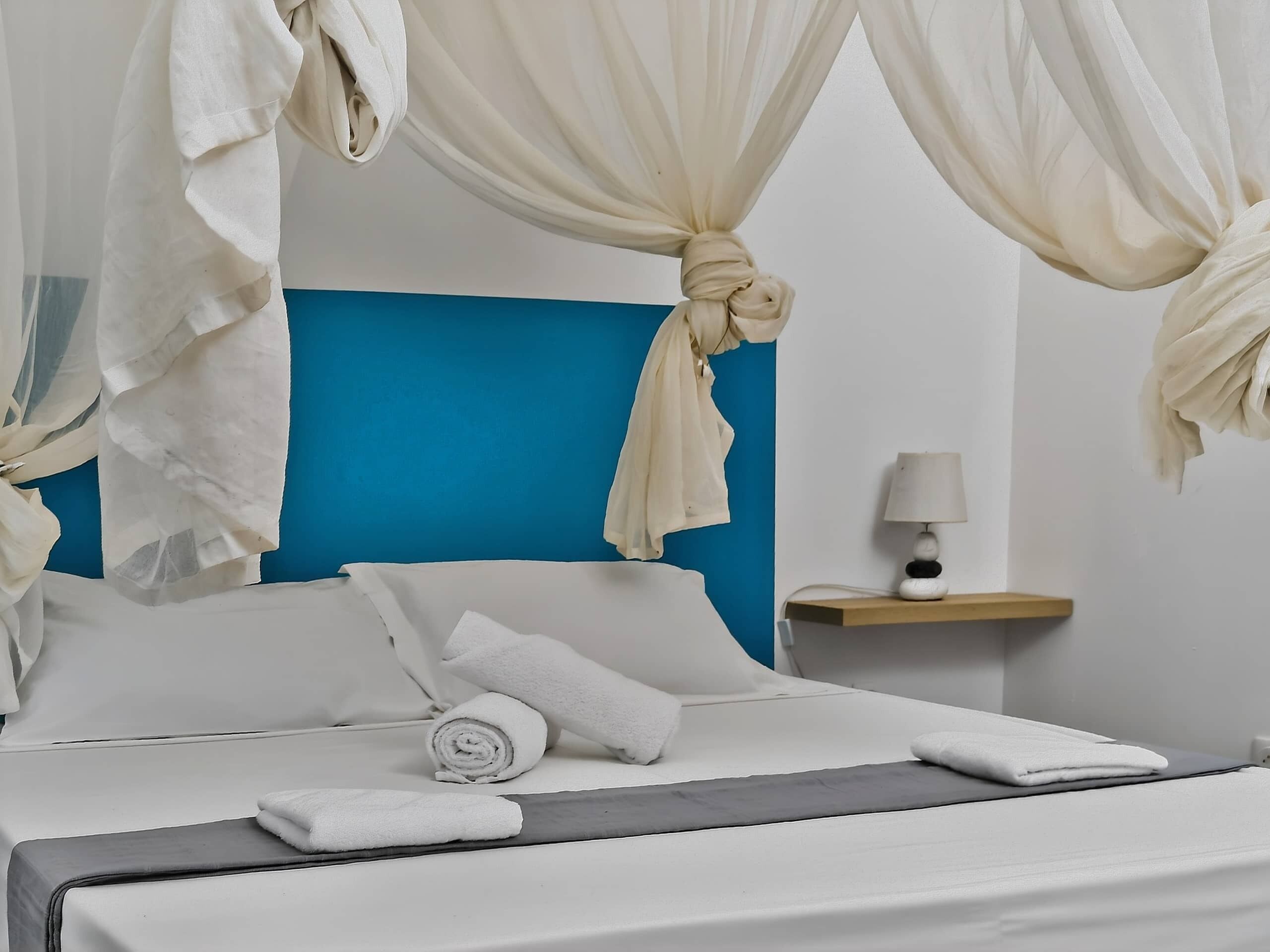 Un lit avec du linge de lit blanc, un mur d’accent bleu et une table de chevet avec une lampe.