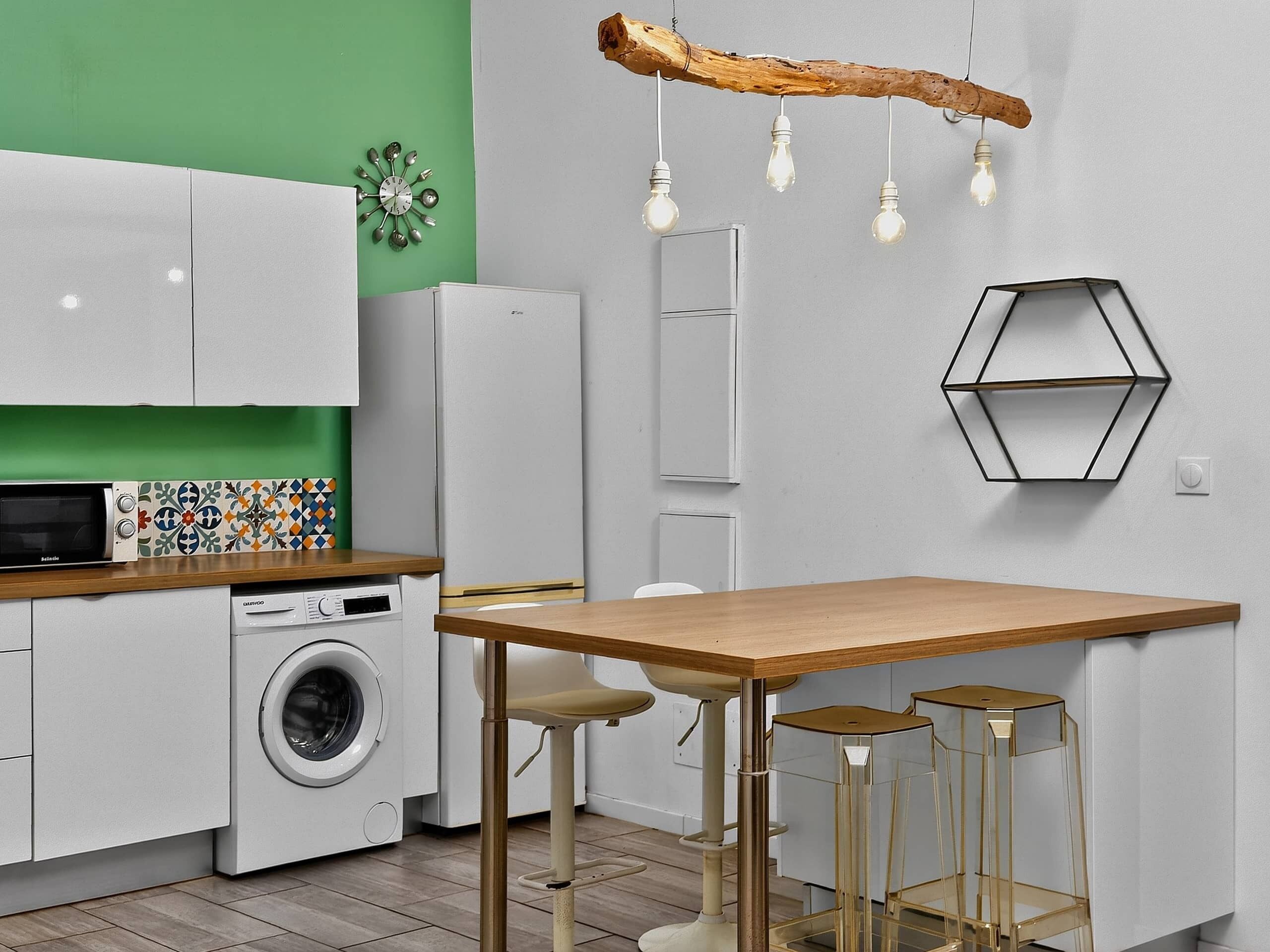 A compact kitchen with a washing machine, a microwave, a wooden table, and bar stools.