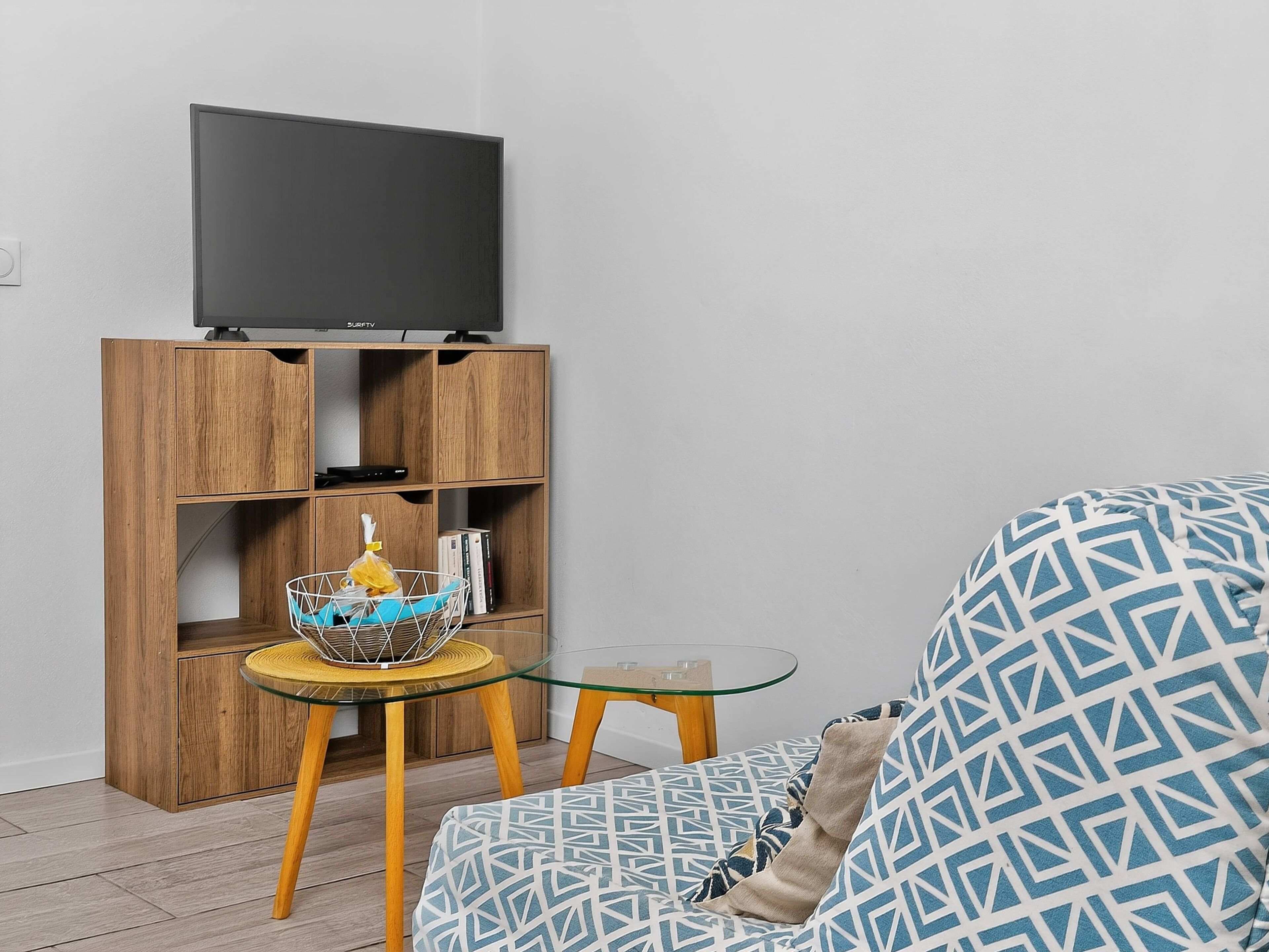 A living room with a sofa, a glass coffee table, a wooden TV stand, and a small side table.