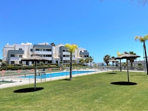 Ein modernes Hotel mit Swimmingpool, Palmen und blauem Himmel.