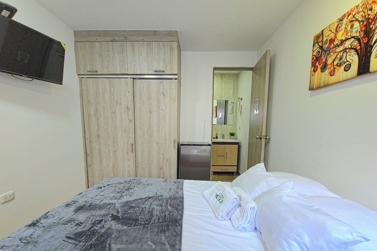 Et hotelværelse med seng, garderobe, lille køleskab, badeværelse med spejl og et billede på væggen.