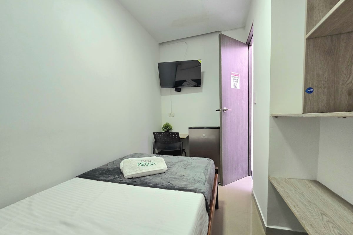 Et lille, moderne hotelværelse med seng, skrivebord, fjernsyn og garderobeskab.