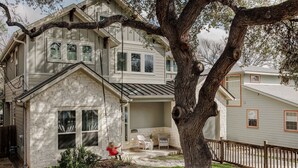 A two-story house with a brick exterior, a covered porch with chairs, and a large tree in the foreground. - SoCo Craftsman ~ Walk to Shops, Cafés, Parks (Austin)