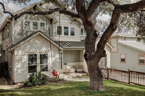 Ein zweistöckiges Haus mit Backsteinfassade, einer überdachten Veranda mit Sitzgelegenheiten und einem großen Baum im Vordergrund.