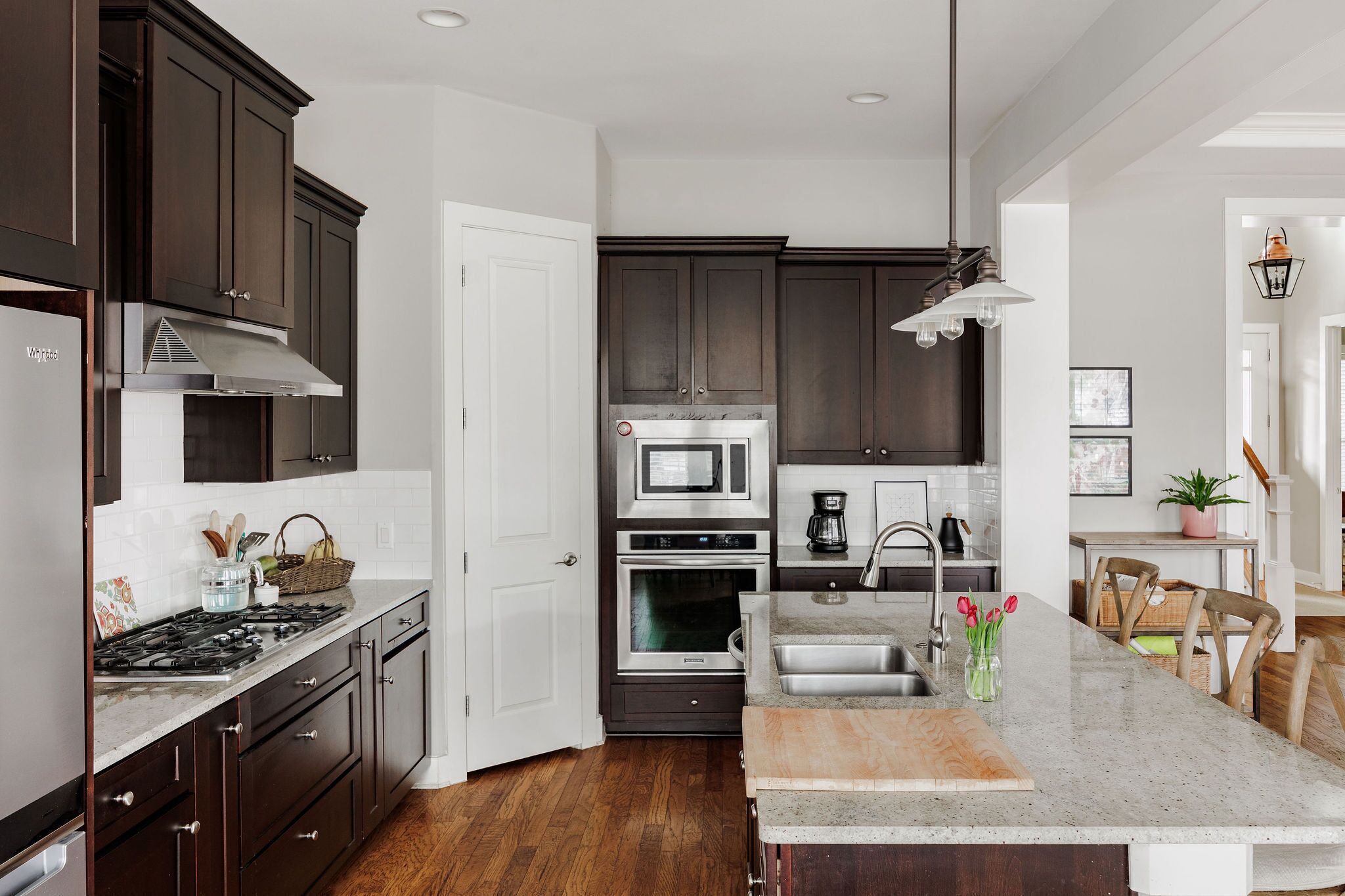A modern kitchen with dark cabinets, stainless steel appliances, a central island with a sink, and a hanging light fixture.