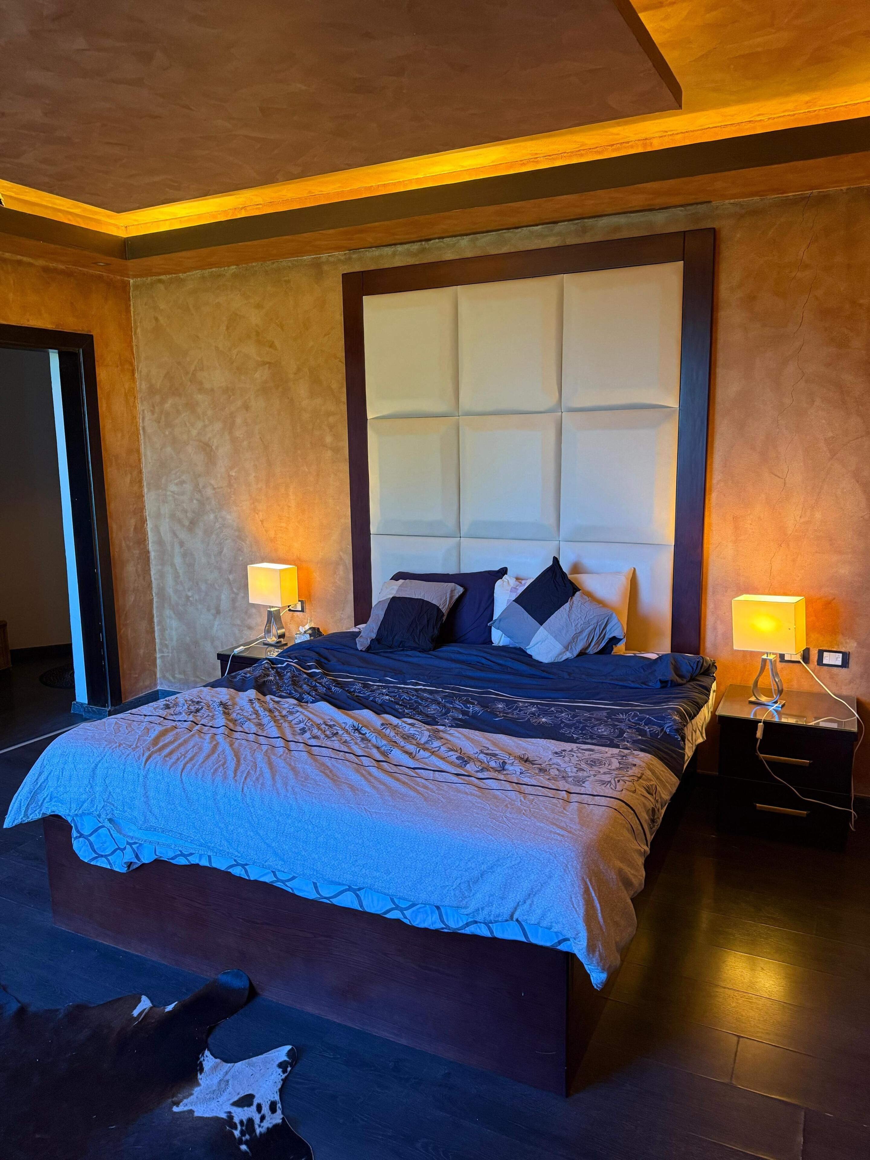Ein Schlafzimmer mit einem großen Bett, zwei Nachttischen mit Lampen, einem Kopfteil und einem Kuhfellteppich.