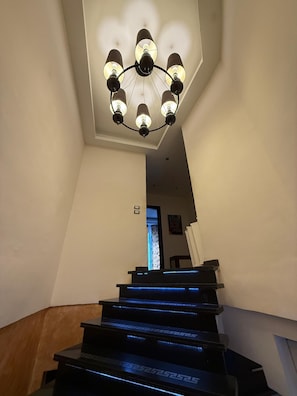 Eine Treppe mit blauen LED-Leuchten, eine Chandelüster mit mehreren Lampen und eine Tür oben.