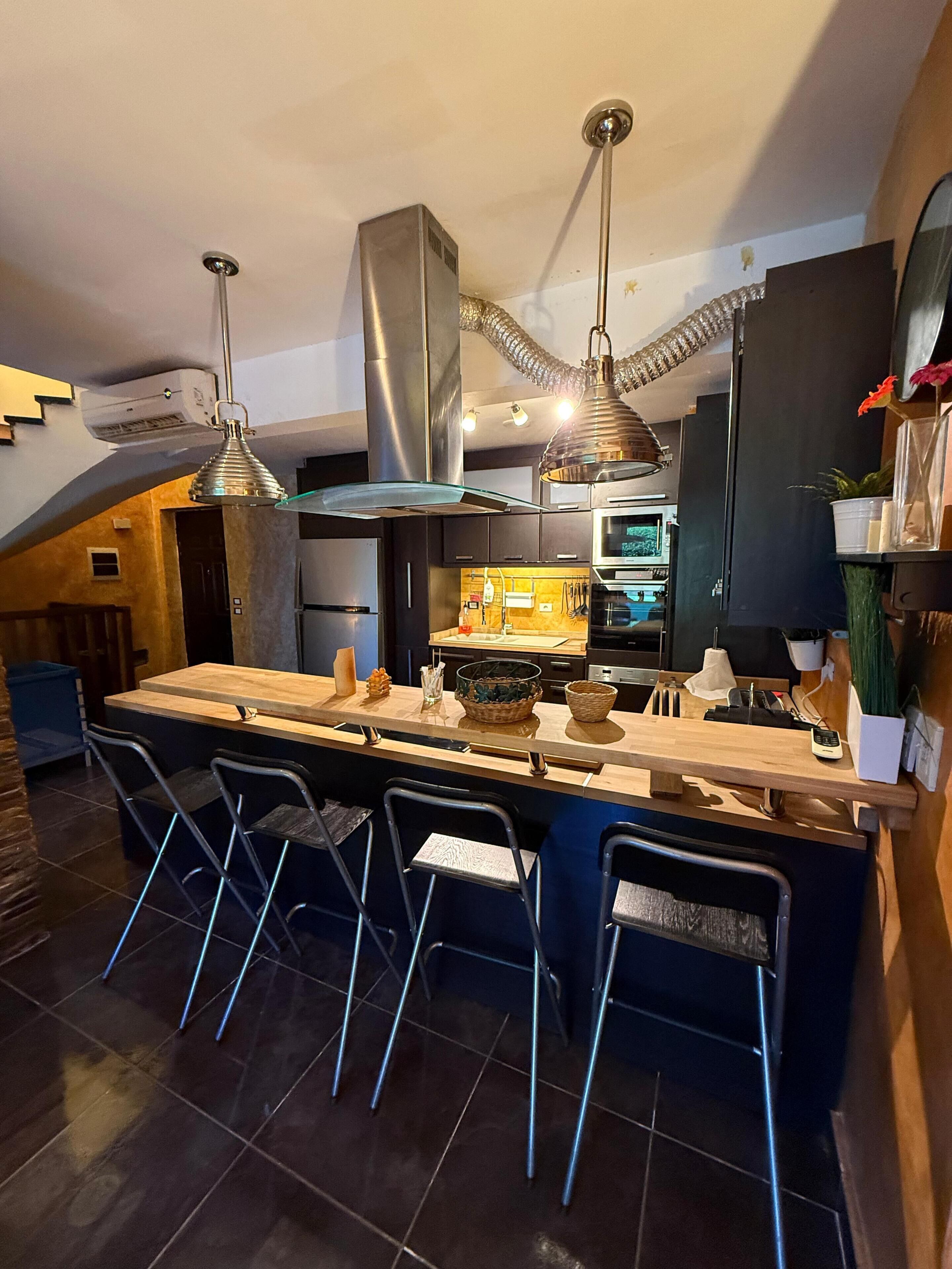 Una cocina moderna con una isla central, taburetes de bar, electrodomésticos de acero inoxidable e iluminación colgante.