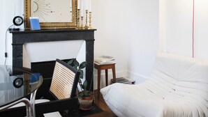 Et værelse med en sort pejs, en hvid sofa, et spejl med billeder og en hængende lyspære.