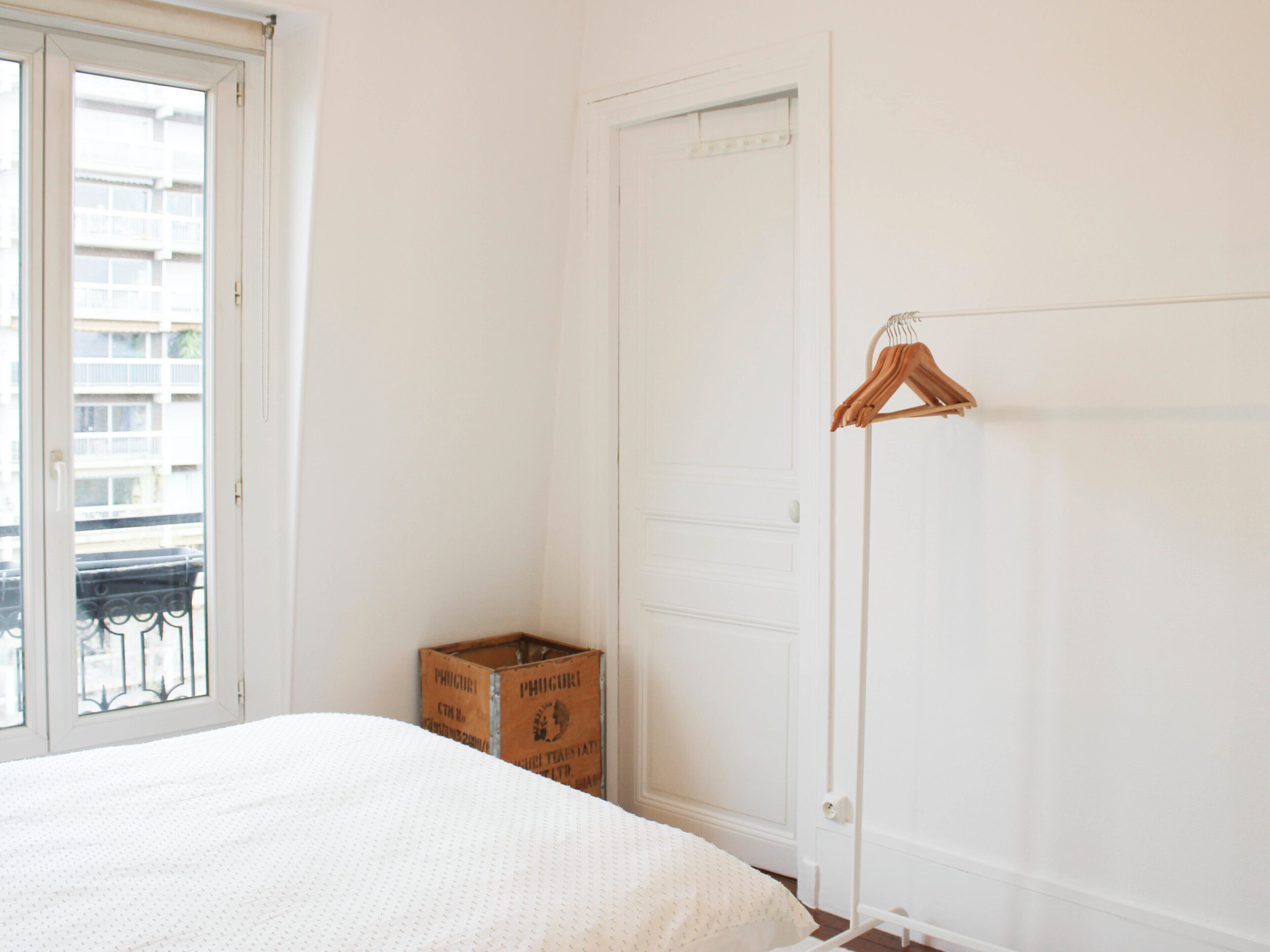 Una camera da letto con un letto, una porta, una finestra e un appendiabiti.