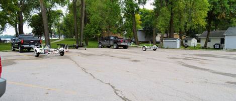A parking lot with several vehicles, including a truck and a trailer, and a row of houses in the background.