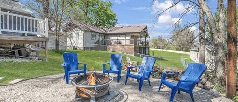 Un jardin avec un foyer, quatre chaises Adirondack bleues et une maison en arrière-plan.