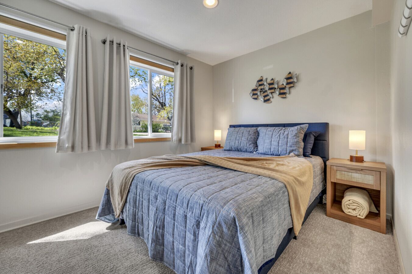 A bedroom with a bed, curtains, a nightstand, a lamp, and a wall decoration.
