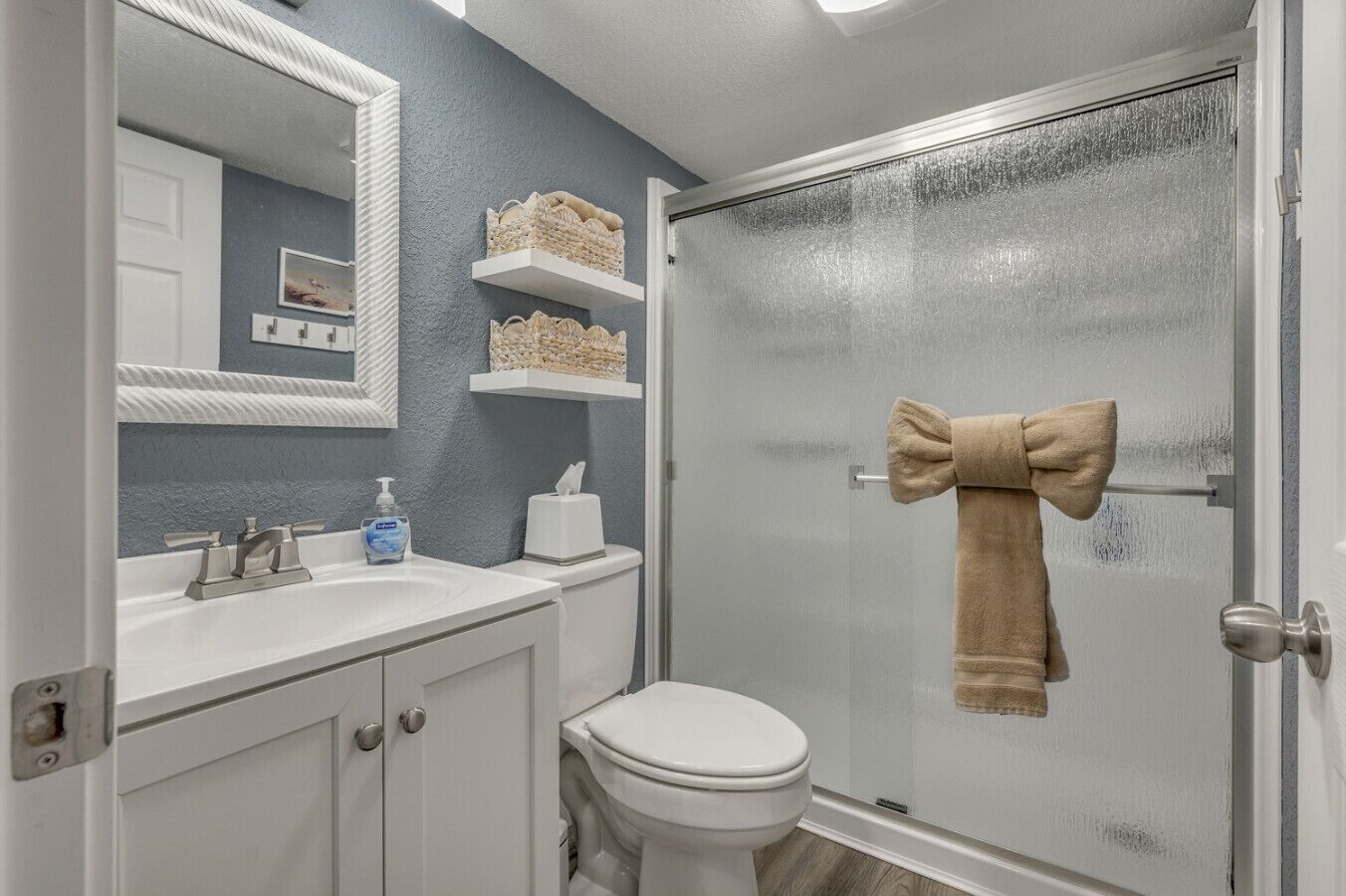 Une salle de bain avec un lavabo blanc, un miroir, des toilettes et une porte de douche.